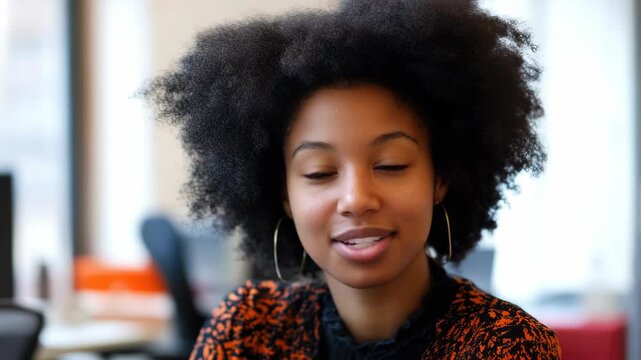 A cheerful woman with an afro smiling for the camera in a modern office environment.