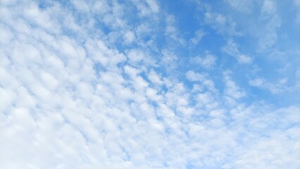 Beautiful natural sky with floating white clouds. Clear blue summer sky as a background texture. Blue sky pattern with soft and airy clouds.