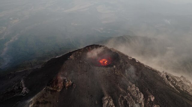 Aerial view of Fuego Volcano crater with glowing lava and steam rising over the surrounding Guatemalan landscape.