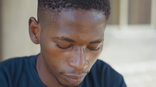 Black man closeup at house doorway focusing on task, tight frame reveals dust and perspiration on skin, navy shirt, shallow depth of field with soft bokeh, concentrated expression, implied roles
