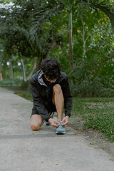 Fototapeta premium Portrait of handsome asian man posing fixing shoelace lace on his running shoe after exercising outdoors. Vitality and activity concept.