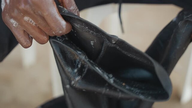Black hands wringing black fabric closeup, fingers inspecting seams and removing residue, lint and texture highlighted, careful squeezing and rubbing to restore garment, patient domestic care