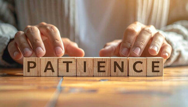 A person's hands holding wooden blocks spelling out the word PATIENCE