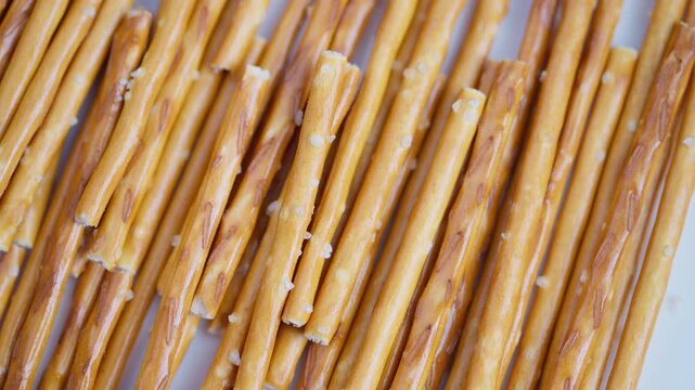 Closeup salted pretzel sticks arranged in tight rows showing golden baked texture and scattered salt crystals, studiolit minimal background, food still life, crisp crunchy snack
