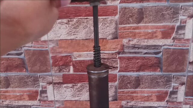 Footage of an antique metal manual air pump with a red pressure tank and rubber hose, placed on a rustic-style stone wall