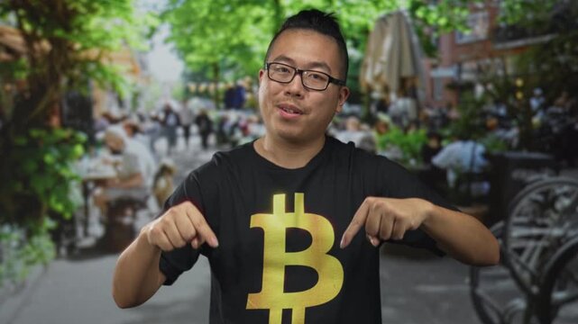 Man in black bitcoin tshirt pointing finger to logo on street terrace restaurant outdoors; crypto confidence.