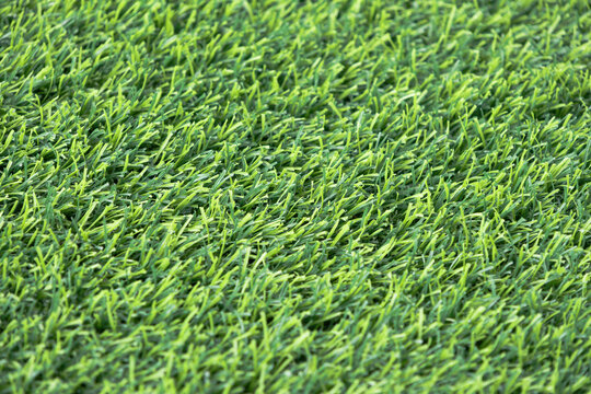 close-up of a lush, green artificial turf. The synthetic blades of grass are perfectly aligned and create a uniform
