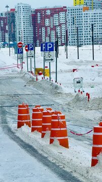 Winter driving school practice area with orange traffic cones and road signs in snow. Driving lessons and safety training at an icy outdoor circuit in the city during cold seasonal weather.