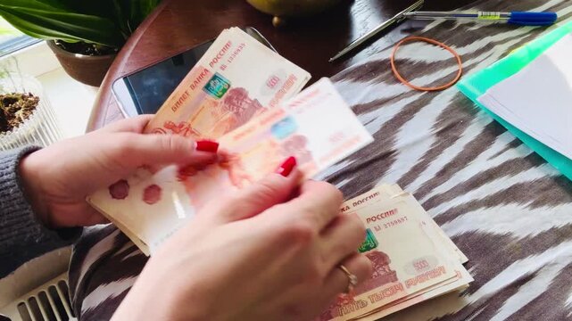 Female hands with beautiful red manicure counting five thousand Russian ruble banknotes at a desk. Concept of wealth, salary, financial success, and cash savings with a focus on feminine style.