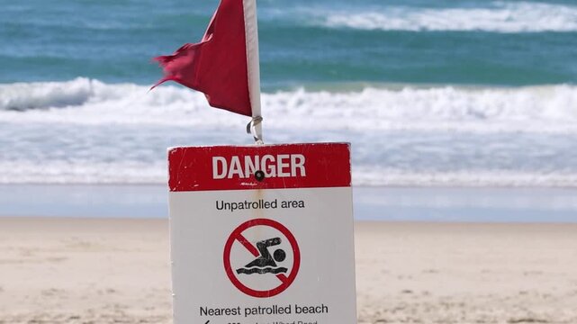 Red Danger Sign and Warning Flag on Sandy Beach with Waves