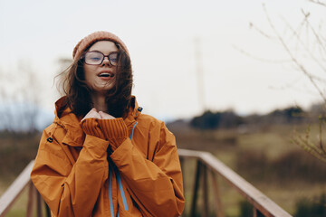Young woman lifestyle outdoors in autumn wears orange jacket and knitted hat, smiling with glasses...