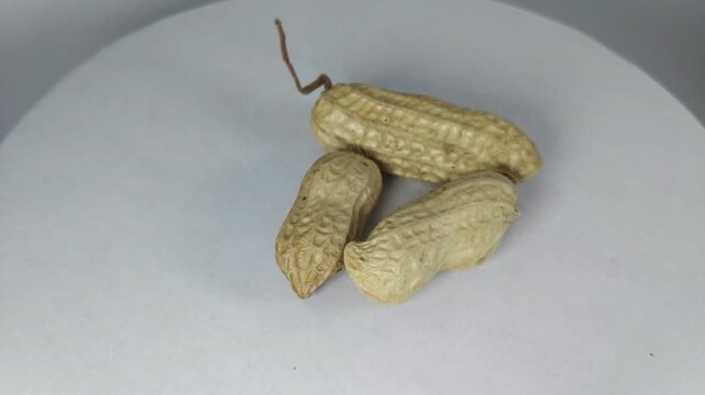 video of raw peanuts complete with covered skin, rotating slowly. Viewed from the top corner, the background is white.