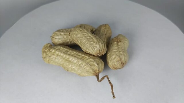 video of raw peanuts complete with covered skin, rotating slowly. Viewed from the top corner, the background is white.