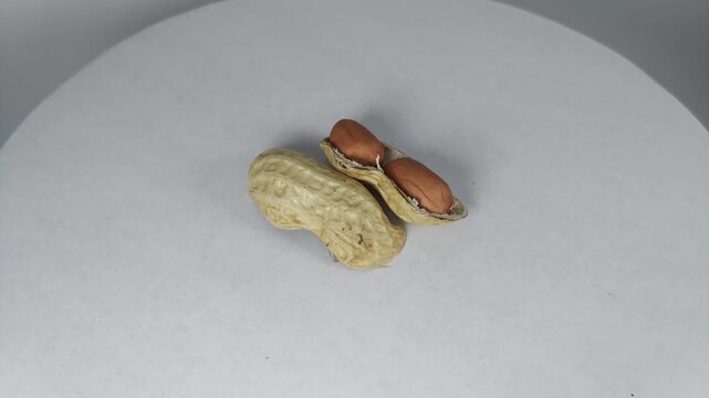 video of raw peanuts complete with exposed skin, rotating slowly. Viewed from the top corner, the background is white.