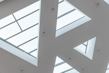 A modern minimalist ceiling features geometric triangular skylights that flood a contemporary...