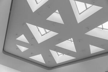 A modern minimalist interior features white geometric triangular skylights, emphasizing clean lines, negative space and architectural abstraction. Black and white photography © evannovostro