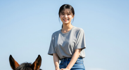 青空の下で馬に乗り、晴れやかな笑顔を見せる乗馬体験中の女性