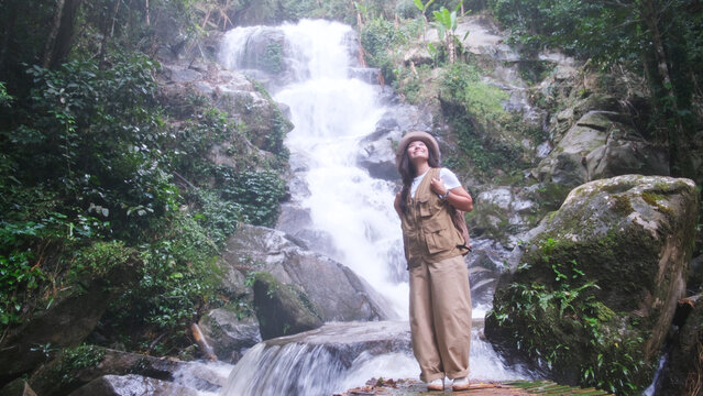 Portrait image of a woman standing in front of the waterfall in the forest