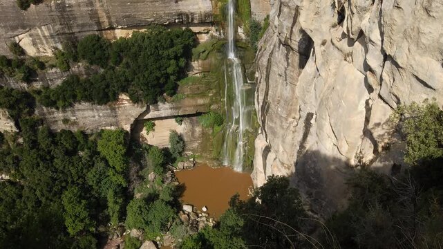 Breathtaking high angle perspective of the Salt de Sallent waterfall cascading down a sheer rock cliff into a natural pool surrounded by a dense green forest in Rupit, Catalonia, Spain