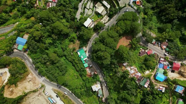 Scenic aerial bird's eye view of winding hillside road amid dense greenery and scattered homes - Benguet, Philippines