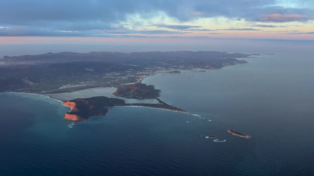 Elevated left side view of Ibiza island captured at sunset from an airplane cockpit, with a view of the city, harbor and the airport runway illuminated by the golden hour light.