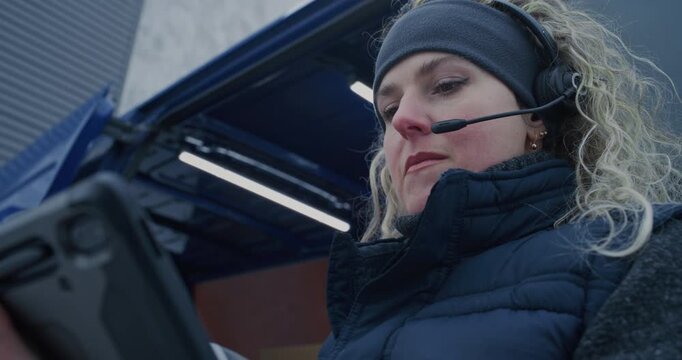 During Snowfall, Logistics Workers Unload Packages From Vehicle. Woman in Headset Manages Scanning and Digital Records on Tablet, Man Transfers Boxes. Modern Supply Chain Work Despite Harsh Weather.
