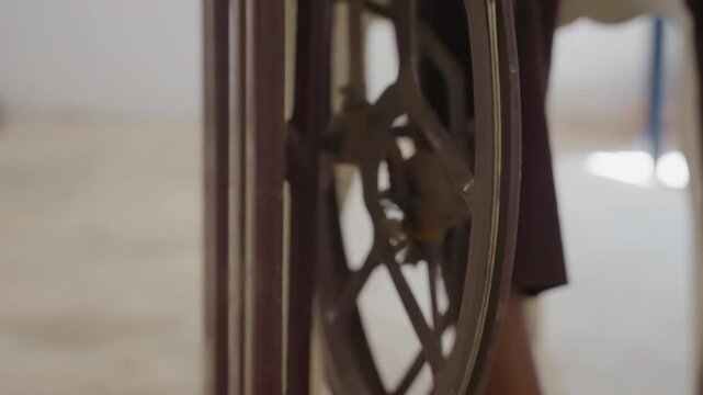 Closeup sewing wheel with black cloth, bright interior framing antique flywheel and wooden frame, implied dressmaker action adjusting fabric and pattern, lively domestic repair scene with focused