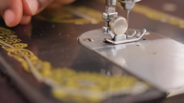 Closeup hand guiding fabric under needle with black sewing machine bed and gold decal precise stitchwork, domestic repair chore in calm home setting, steady rhythm of presser foot and thread tension,