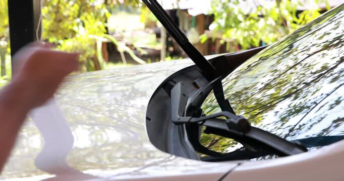 Close up male hand lowering the windshield wiper blade onto the front glass of a white car. Driver preparing vehicle for rainy weather or doing regular auto maintenance. 4K video footage.