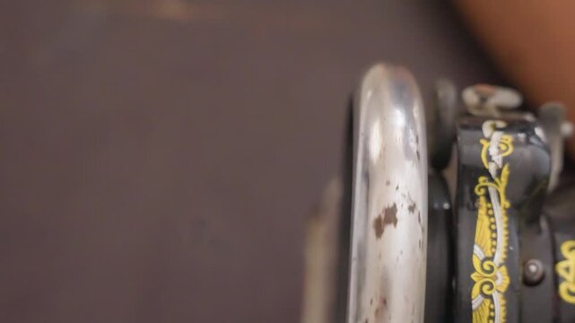 Tight shot black sewing machine wheel capturing slow rotation and chrome wear, rhythmic domestic routine in home sewing corner, muted tones, steady pace, habitual chore atmosphere