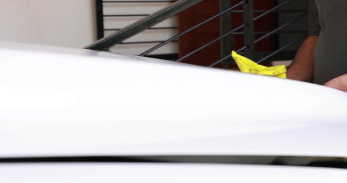 Side view of a male mechanic or driver hands wiping and cleaning the car engine compartment with a yellow microfiber cloth. Auto detailing and vehicle maintenance routine. High quality 4K video.
