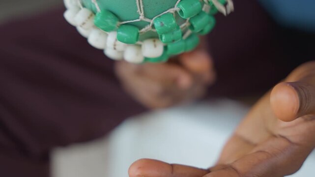 Gentle hands holding textured rattle. Detailed shot of black hands clutching sensory rattle with gentle spin. Upclose perspective showing hands softly grasping and rotating textured beaded rattle