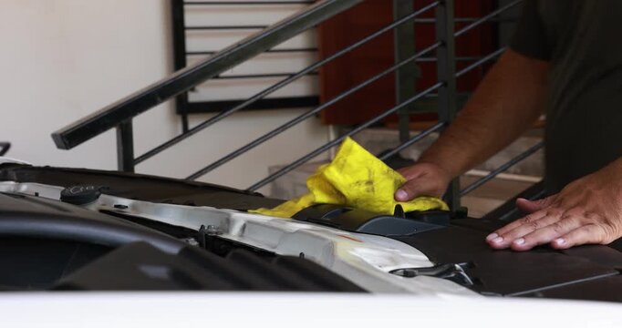 Side view of a male mechanic or driver hands wiping and cleaning the car engine compartment with a yellow microfiber cloth. Auto detailing and vehicle maintenance routine. High quality 4K video.