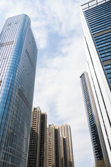 Fototapeta premium Tall modern skyscrapers rise against cloudy sky in urban cityscape with glass facades and reflective surfaces