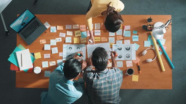 Top view of business team write graphic logo on meeting table with colorful sticky notes and design while explain idea. Project manager sharing idea and explain concept art to smart team. Symposium.