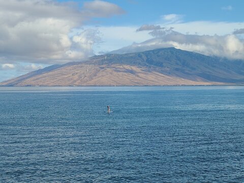 The windward slopes of West Maui mountains are covered in clouds while sun shines on the leeward slopes and windmills fly in the wind