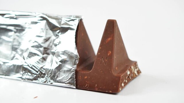 Close up shot of triangular milk chocolate bar with nuts in foil wrapper on white background