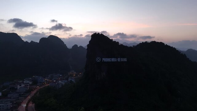 Phong Nha &ndash; Ke Bang National Park, Bo Trach, Quang Binh, Central Vietnam &ndash; 4K aerial drone footage of karst mountains at sunset with illuminated town and iconic Phong Nha sign