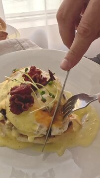 Hand cutting into a croque monsieur, a classic french breakfast dish with eggs, ham and bechamel toppings using fork and knife