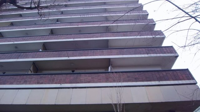 Cinematic upward tilting movement showing the repeating horizontal balcony patterns of a large residential apartment block. Clear architectural detail of urban social housing in a city district.