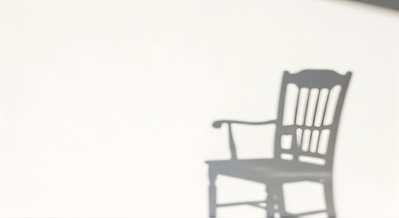 Shadow of a vintage wooden armchair cast on a bright white wall creating a minimalist and abstract composition with a sense of quiet solitude and contemplation