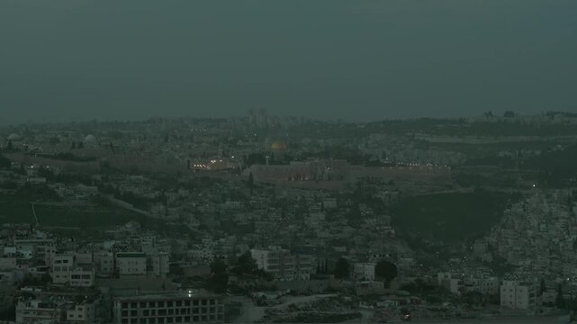 Cinematic twilight view of the historic Old City walls, Dome of the Rock, and Temple Mount in Jerusalem. The holy site sacred to Judaism and Islam is covered in dust during dusk.