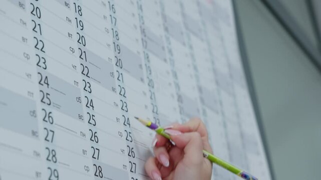 Woman carefully circles date on calendar using pencil. Planning action highlights organization and time management within daily workflow.