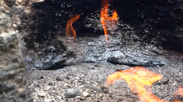 Natural methane gas fire burns between rocks on barren ground across a rugged rocky landscape. Eternal flames rise from stone gaps as subsurface fuel ignites within raw desolate terrain.