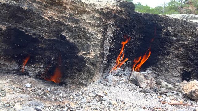 Natural methane gas fire burns between rocks on barren ground across a rugged rocky landscape. Eternal flames rise from stone gaps as subsurface fuel ignites within raw desolate terrain.
