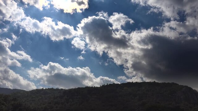 Timelapse clouds drift over forested mountain ridge during humid partly cloudy weather. Moving sky reveals moist air patterns above tree covered hills and natural terrain.