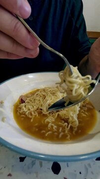 Close-up of gong zai mein or chicken instant noodles being eaten from a bowl with a fork and spoon, iconic staple cafe food in Hong Kong