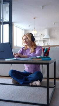 Smart attractive blonde female high school student in wireless headphones preparing for exam, studying distant online course and communicating with teacher while-learning at home.