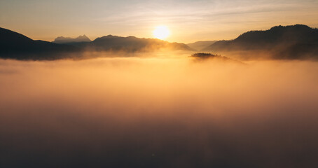 Fototapeta premium Breathtaking aerial view of golden sunlight hitting a sea of fog flowing through mountain ridges at sunrise.