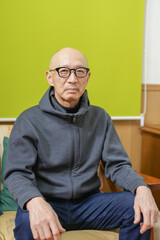 Fototapeta premium An older man wearing glasses and a gray hoodie sits on a couch. He is in a relaxed and comfortable mood